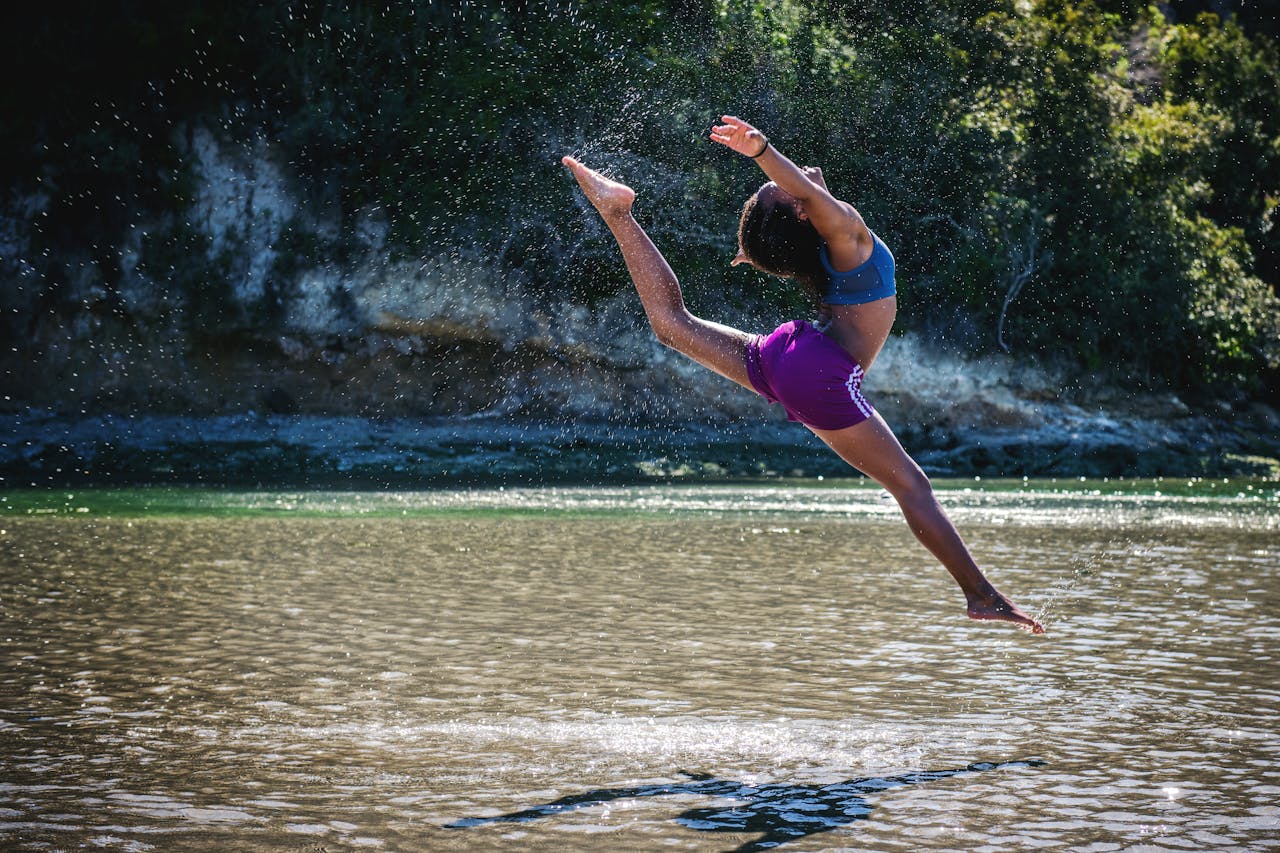 Young woman leaps in front of a river, showcasing flexibility and energy.